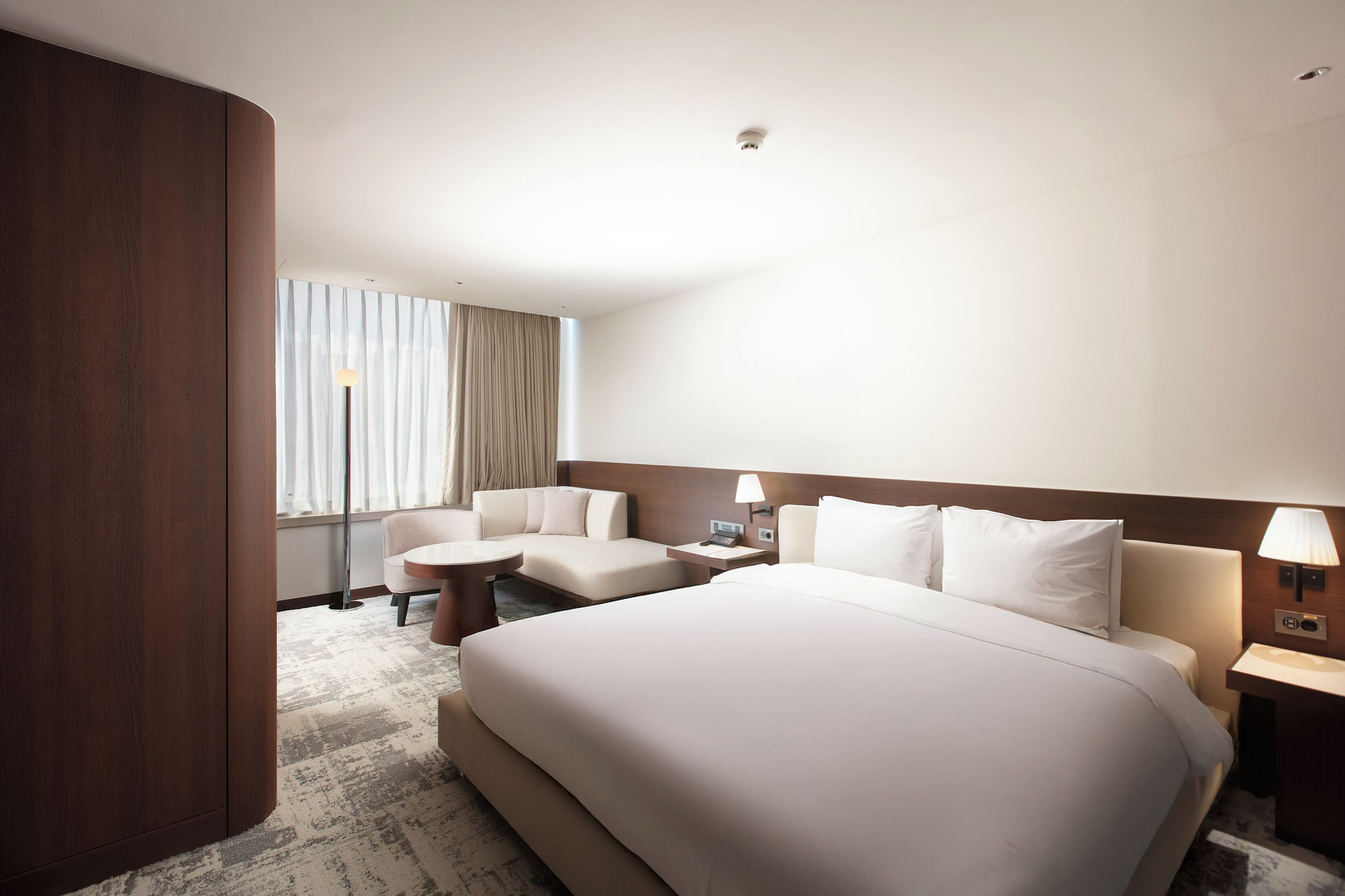 A hotel room with a large bed, a desk, a chair, and a window with curtains.