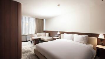 A hotel room with a large bed, a desk, a chair, and a window with curtains.
