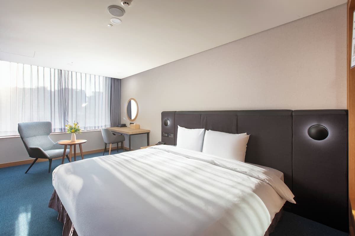 A hotel room with a large bed, a desk, a chair, and a window with curtains.