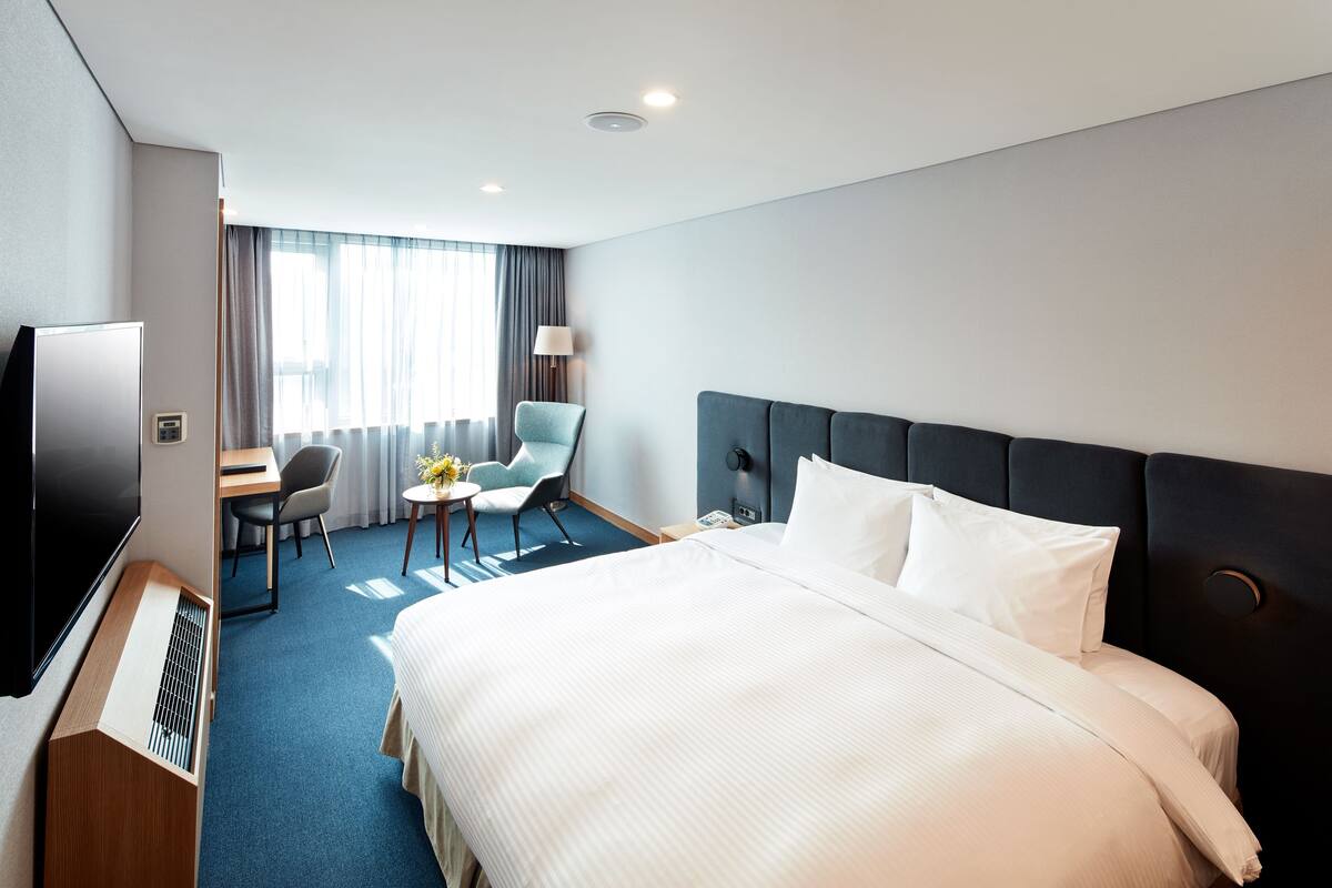 A hotel room with a large bed, a desk with a chair, a TV, and a window with curtains.