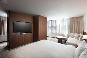 Ett hotellrum med en stor säng, en platt-TV, en soffa, ett litet runt bord och ett fönster med gardiner.