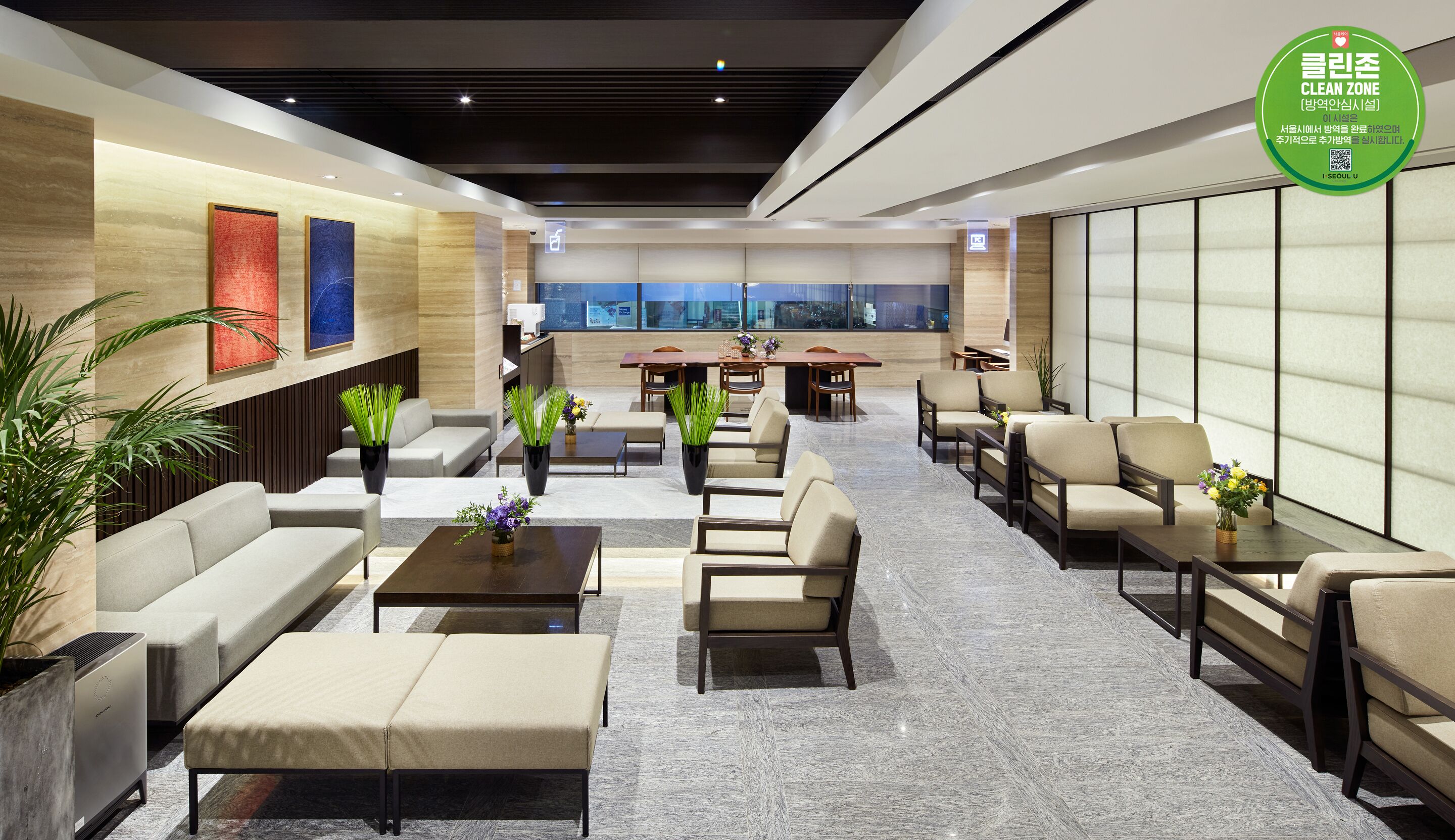 A modern hotel lobby with seating areas, a reception desk, and a large window offering a city view.