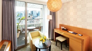 A modern hotel room with a city view, a dining area, and a desk with a lamp.