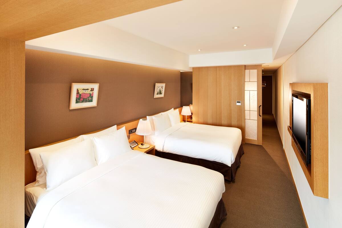 A hotel room with two beds, a TV, and a hallway leading to a bathroom.