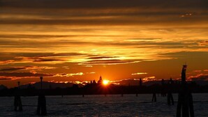 A sunset over a body of water with a silhouette of a city skyline in the background. - Hotel Cristallo (Venice)