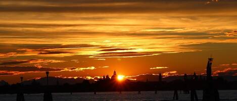 A sunset over a body of water with a silhouette of a city skyline in the background.