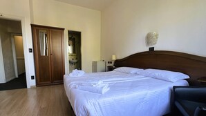A hotel room with a large bed, a wooden headboard, a bedside table with a lamp, and a bathroom visible through an open door. - Hotel Cristallo (Venice)