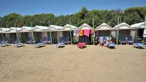 A row of beach huts with blue lounge chairs in front, a red table, and a person sitting on a chair. - Hotel Cristallo (Venice)