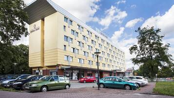 Un hotel con fachada amarilla moderna, varios pisos y un estacionamiento con varios coches.