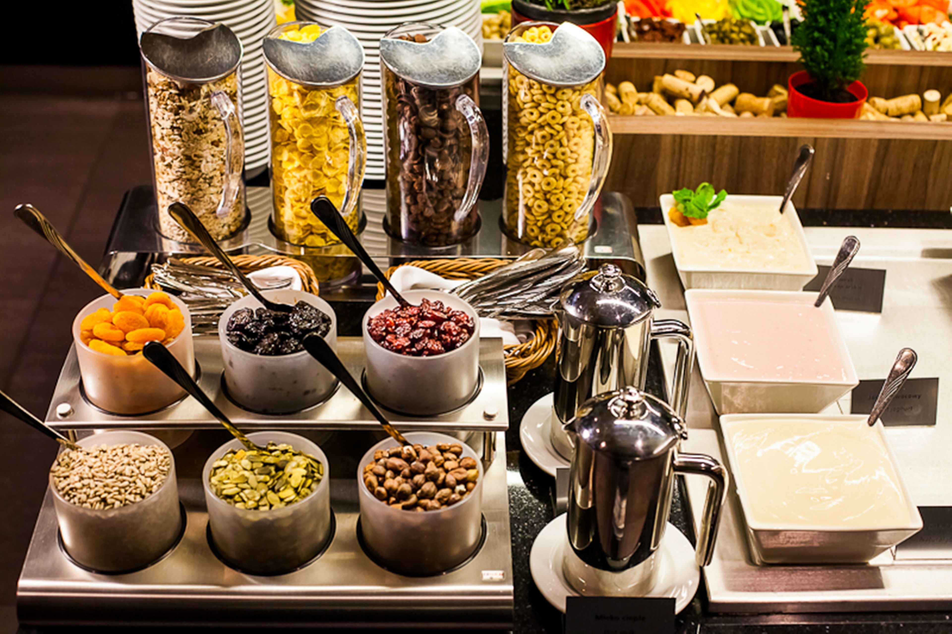 A buffet with various food items in containers, including cereals, nuts, and fruits.