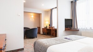 A hotel room with a bed, a desk, a chair, a TV, and a lamp.