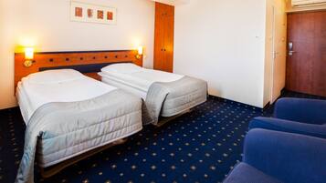 Een hotelkamer met twee bedden, een houten garderobe, een blauw tapijt en een zithoek met blauwe stoelen.