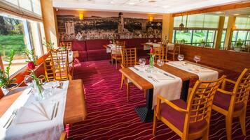 A restaurant with red carpet flooring, wooden tables and chairs, and a mural of a cityscape on the wall.