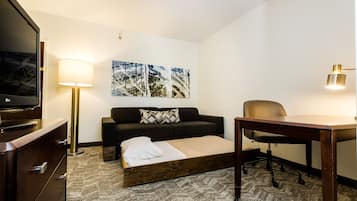 Et hotelværelse med en seng, en sofa, et skrivebord, en stol, et fjernsyn og en lampe.