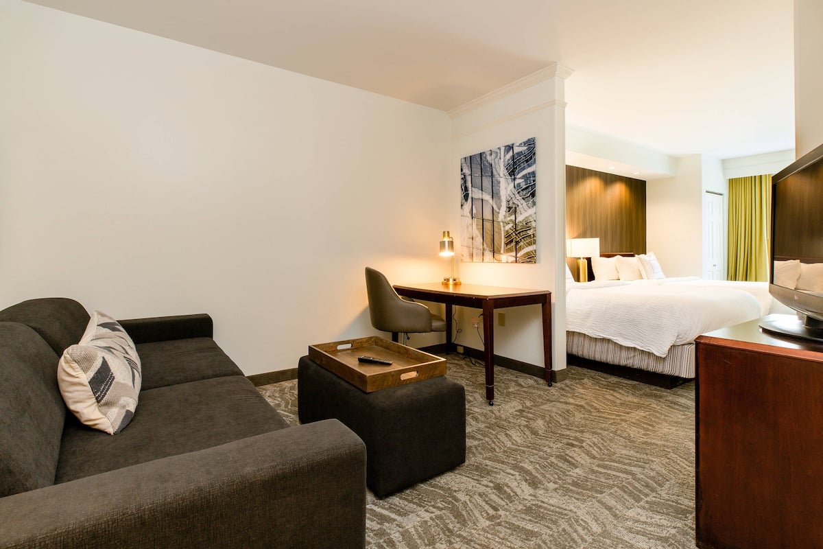 Quarto de hotel com sofá, puf, escrivaninha e cama.