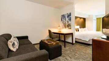 A hotel room with a sofa, ottoman, desk, and a bed.