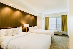 Habitación de hotel con dos camas, un cabecero de madera, una ventana con cortinas y un aire acondicionado instalado en la pared.