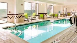 An indoor swimming pool with clear blue water, surrounded by green chairs and a tiled floor.