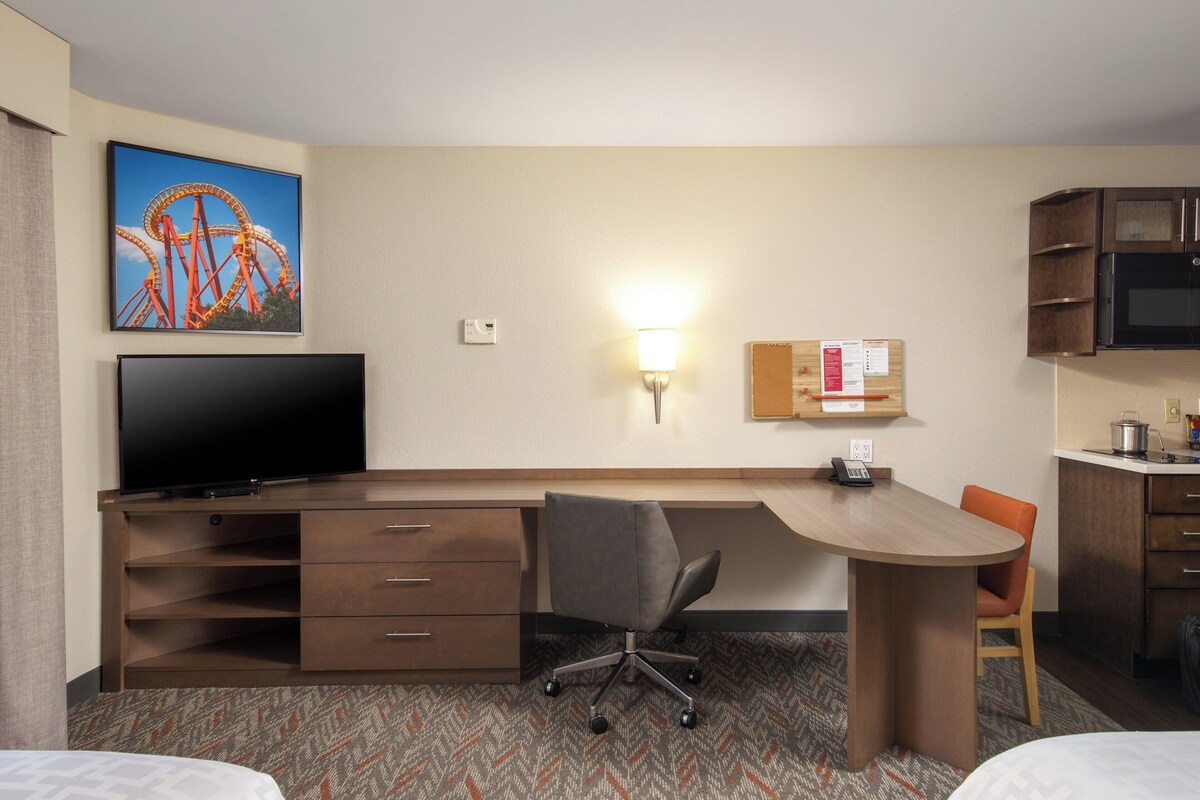 A hotel room with a desk, chair, television, and a wall-mounted light.