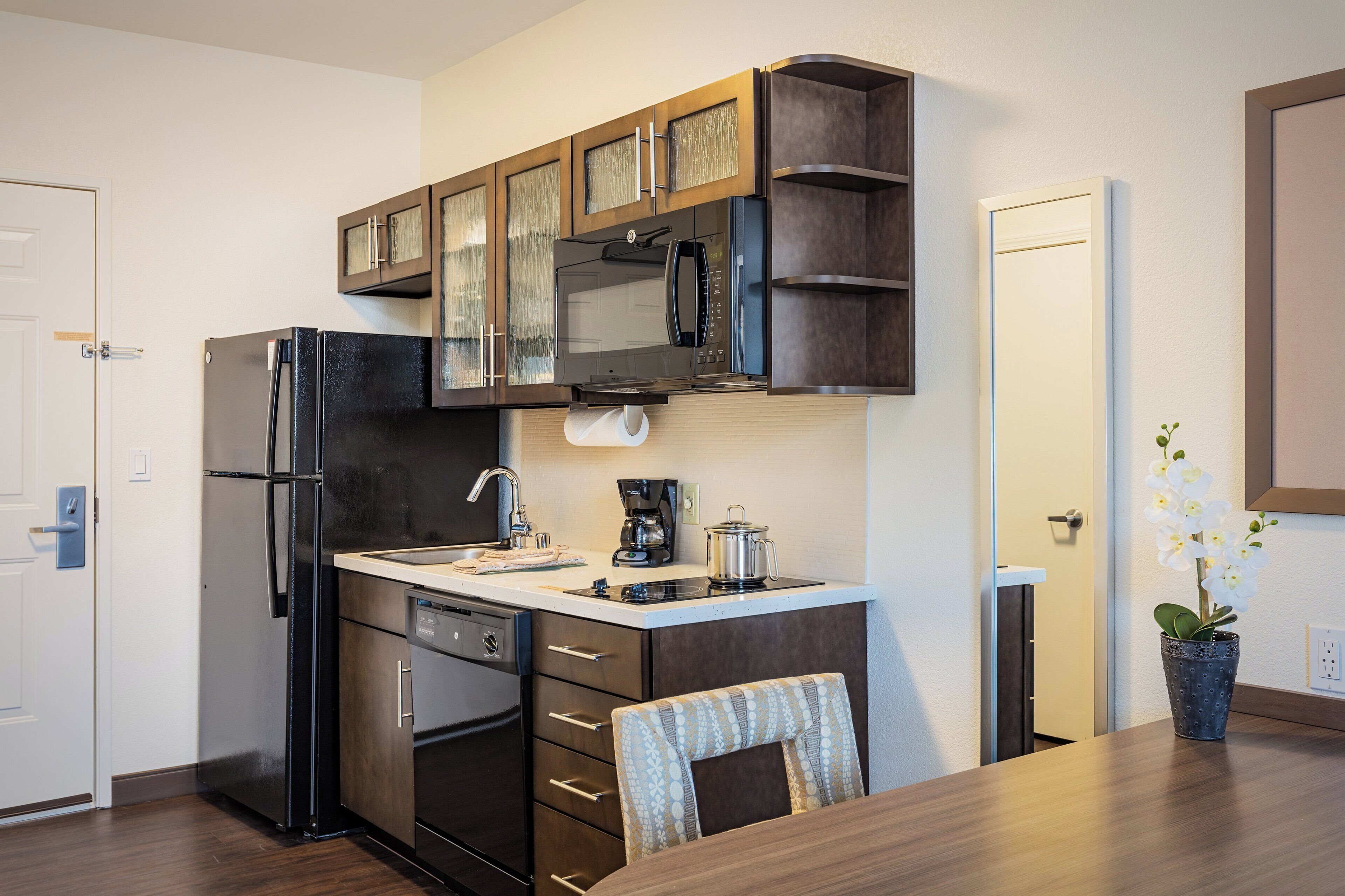 A compact kitchen with a refrigerator, microwave, coffee maker, and a small dining table.