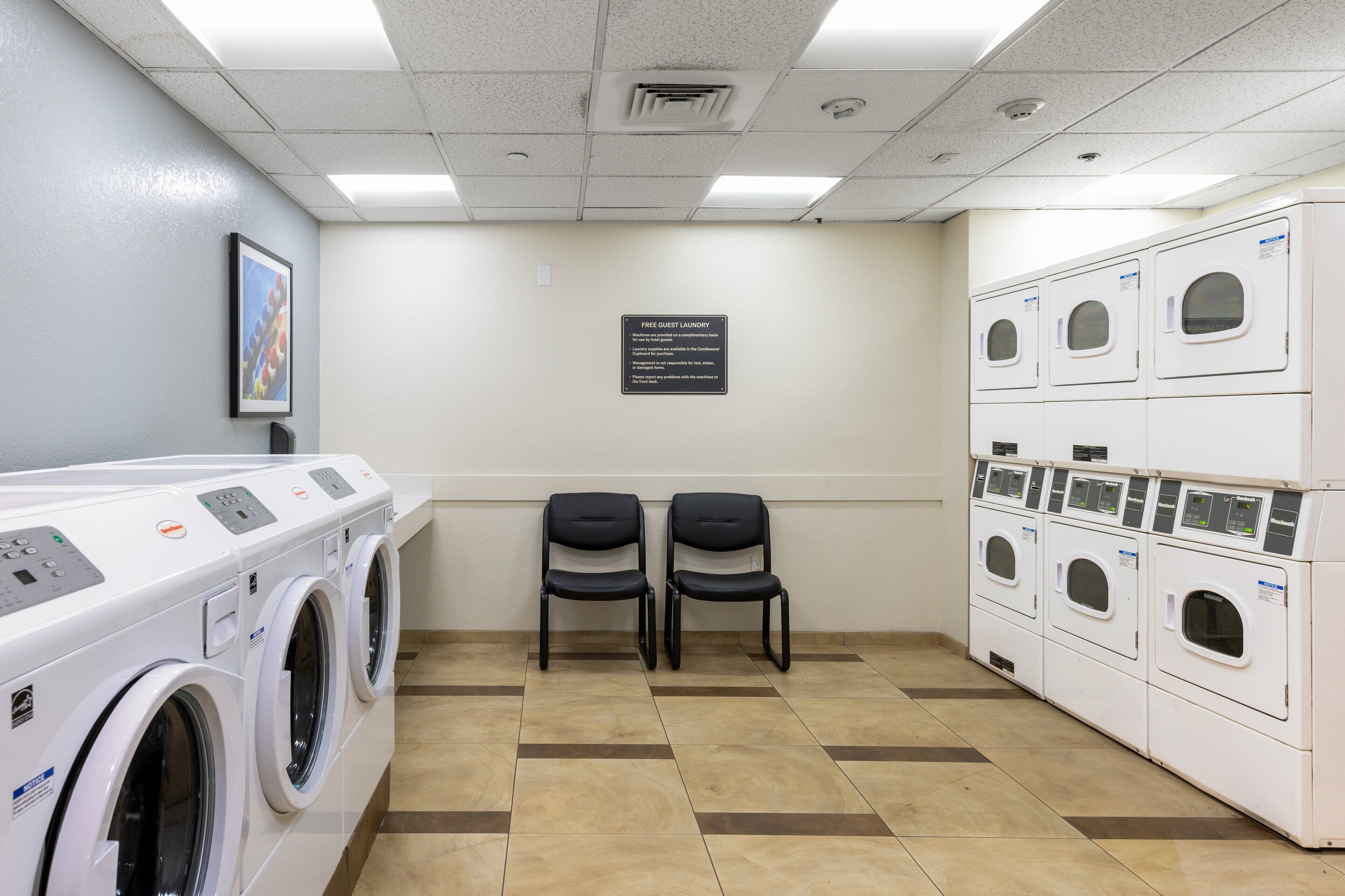 A laundry room with multiple washing machines, two chairs, and a sign indicating free guest laundry.