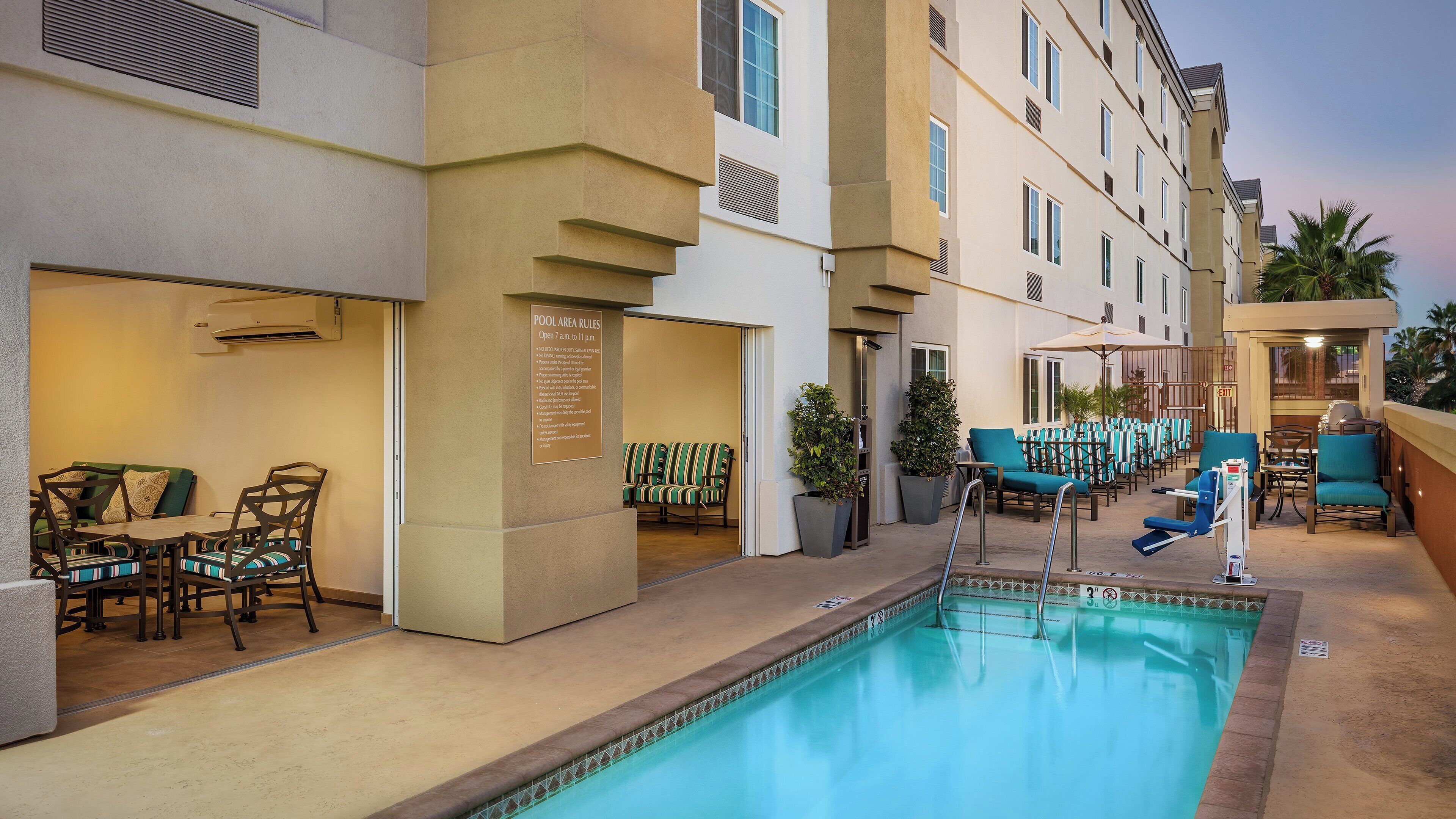 Un área de piscina de hotel con sillones de descanso y una mesa junto a la piscina.