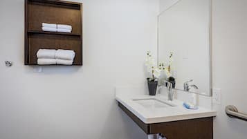 A bathroom with a white sink, two faucets, a mirror, and a wooden shelf with folded towels.