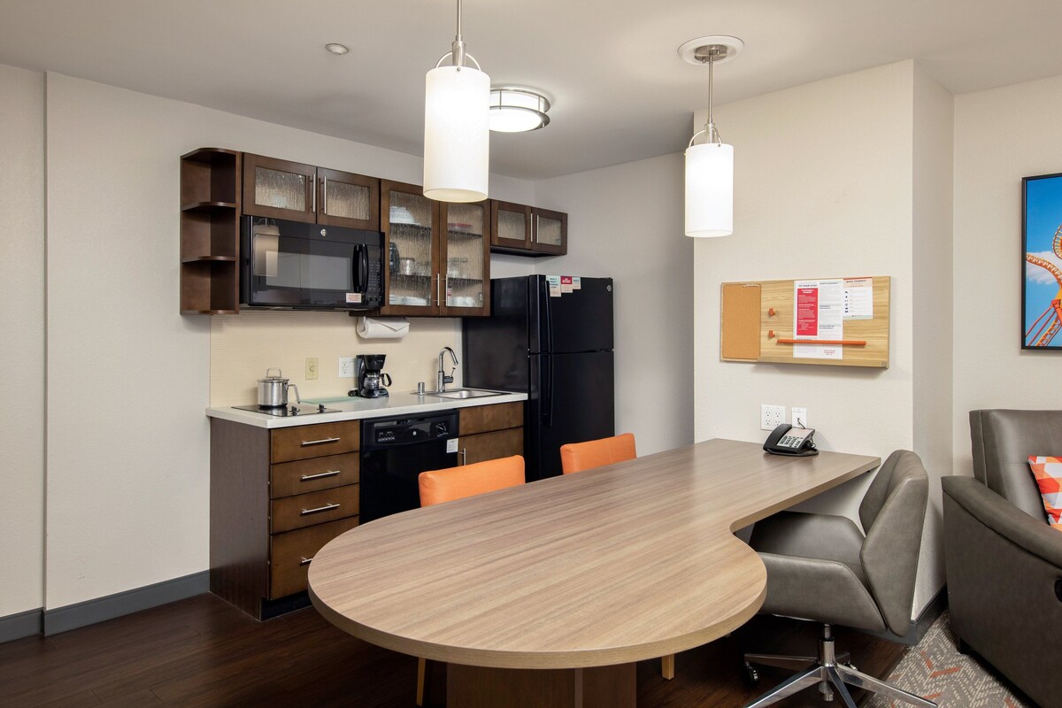 A modern kitchen with a dining area, including a wooden table and chairs, a refrigerator, and cabinets.