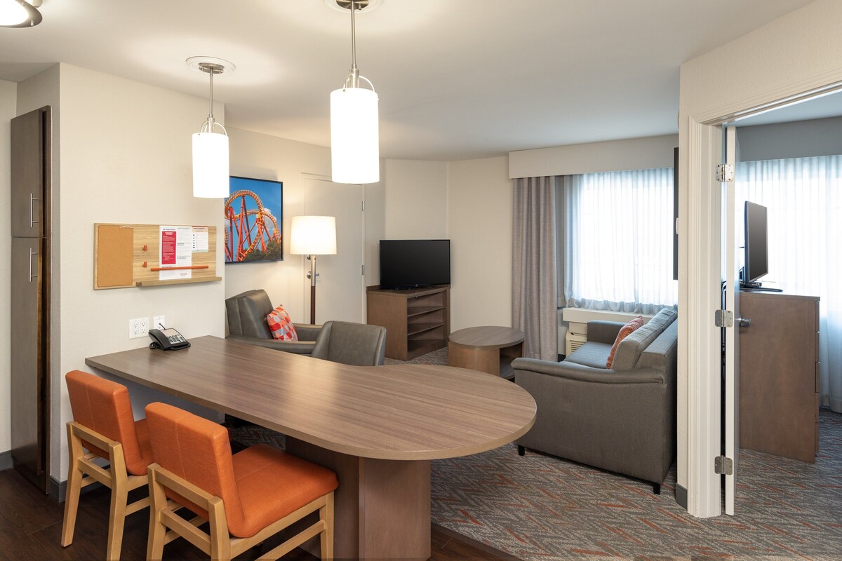 A hotel room with a dining area, a sofa, a TV, and a door leading to another room.