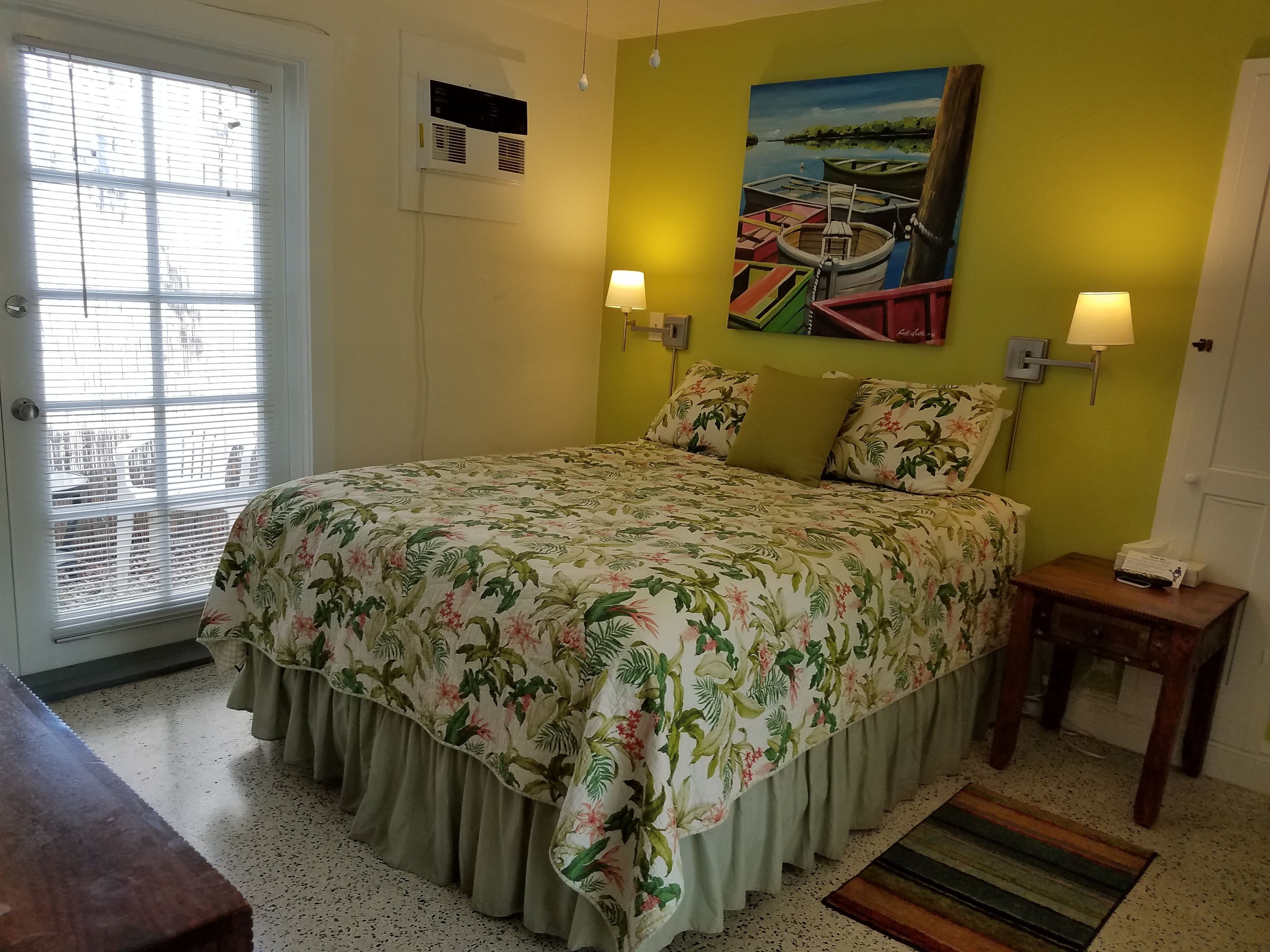 A bedroom with a floral bedspread, a painting of boats on the wall, and two bedside lamps.