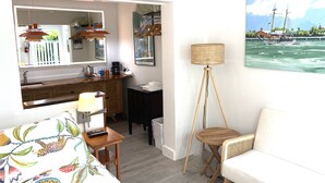 A room with a bed, a desk, a chair, a lamp, a painting of a boat on water, and a view of the sea.