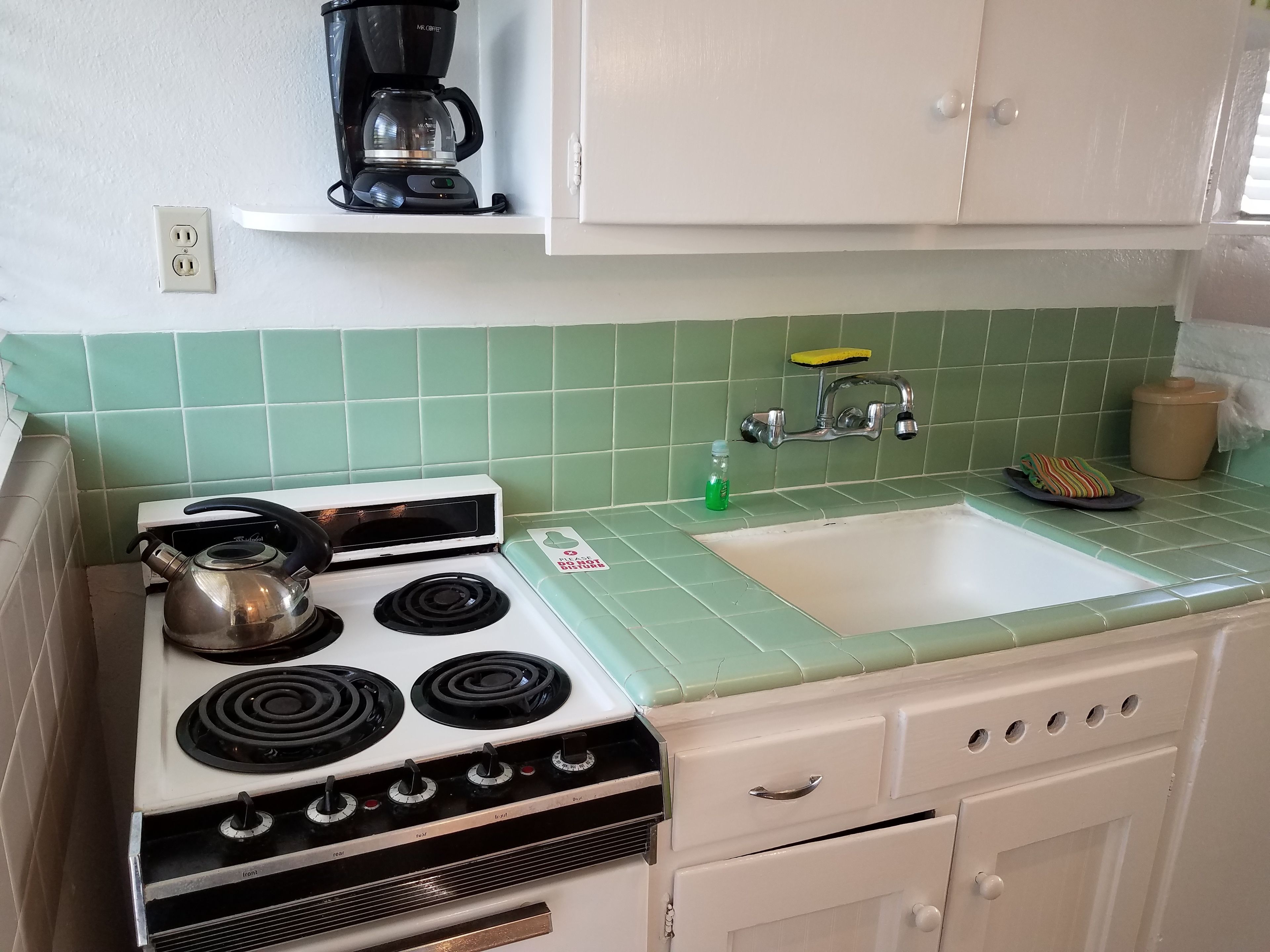 A kitchen with a stove, sink, and a coffee maker on a shelf.