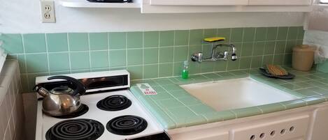 A kitchen with a stove, sink, and a coffee maker on a shelf.