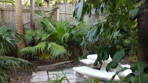 A garden with a stone pathway, a wooden fence, and various tropical plants.