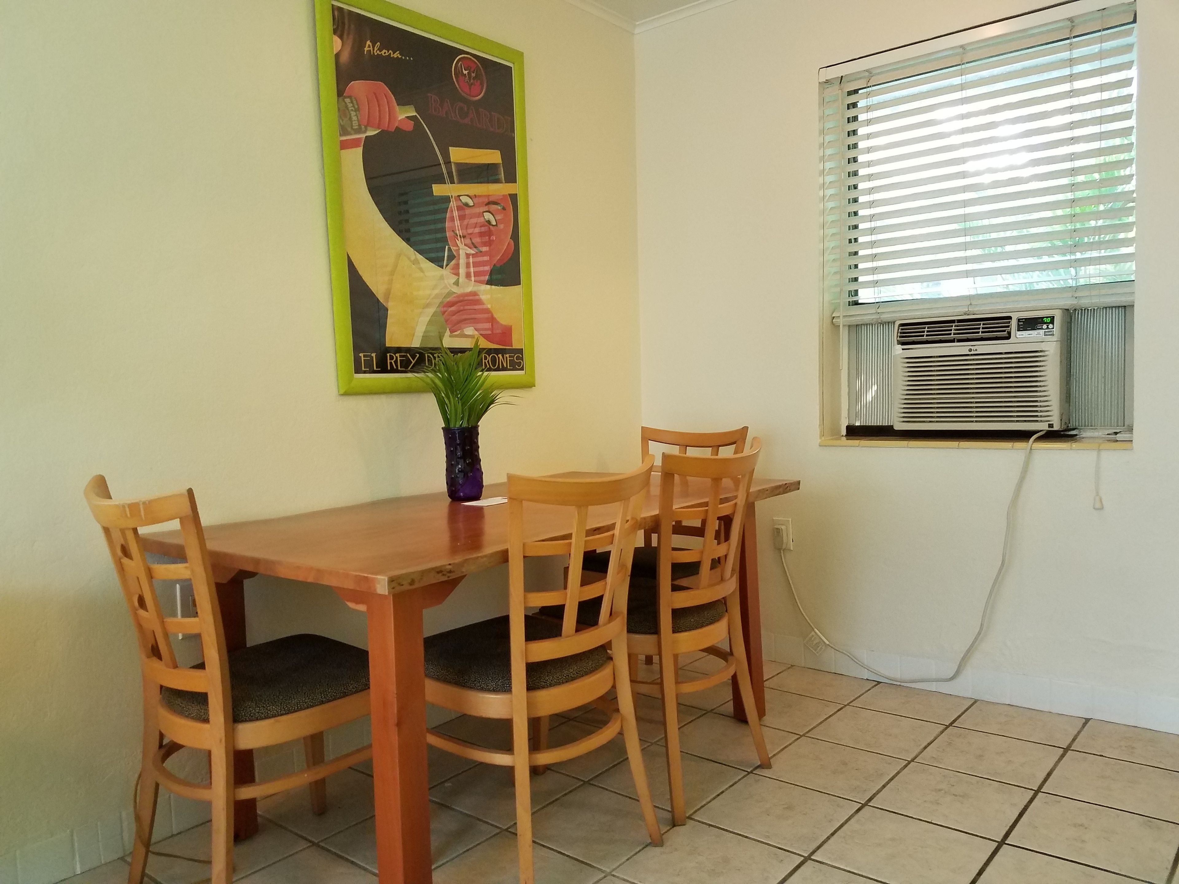 Un coin repas avec une table en bois et quatre chaises, une plante en pot et un climatiseur fixé au mur.
