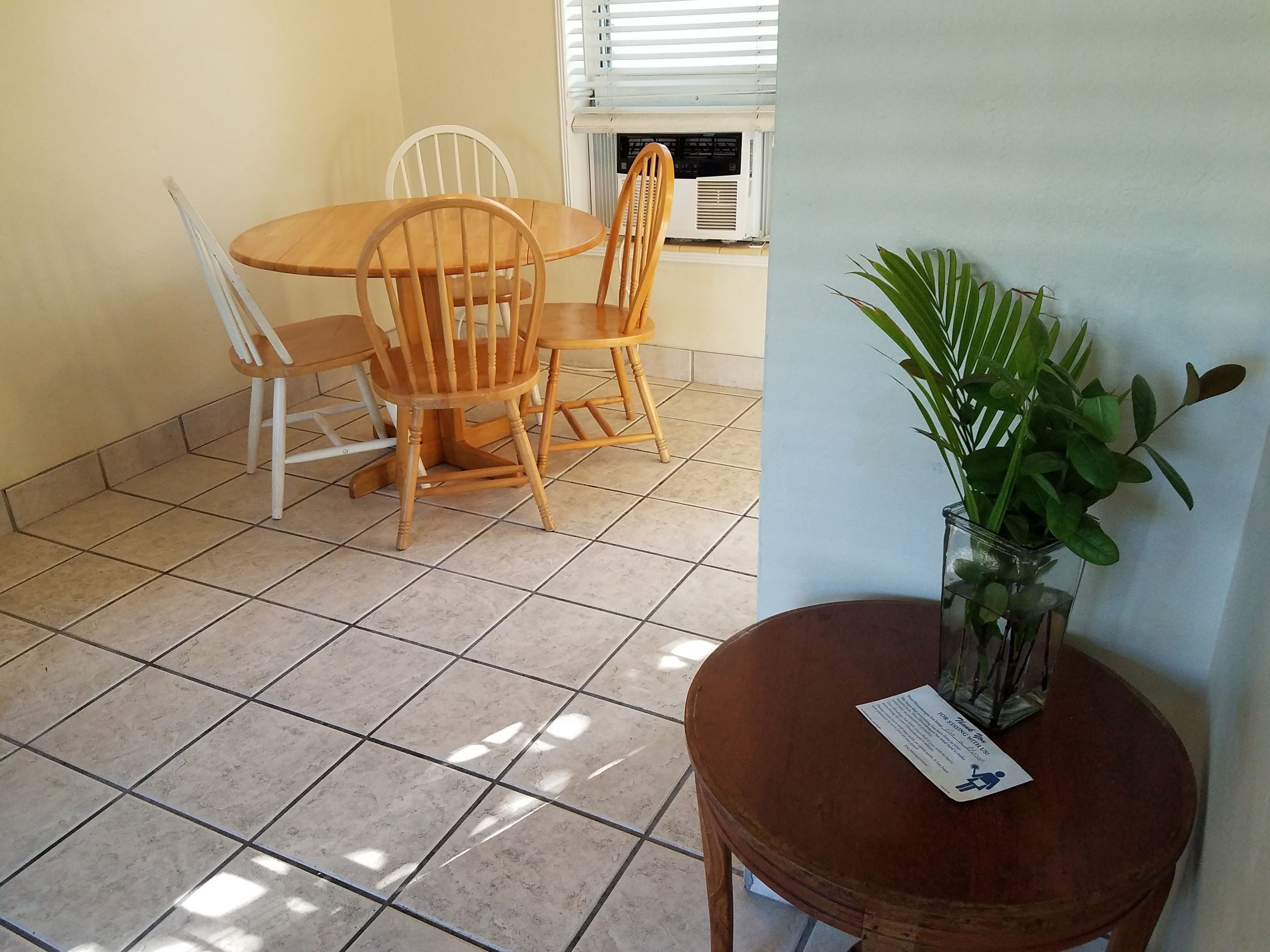 A dining area with a round wooden table and four wooden chairs. There is a potted plant on a small wooden table next to the dining area.
