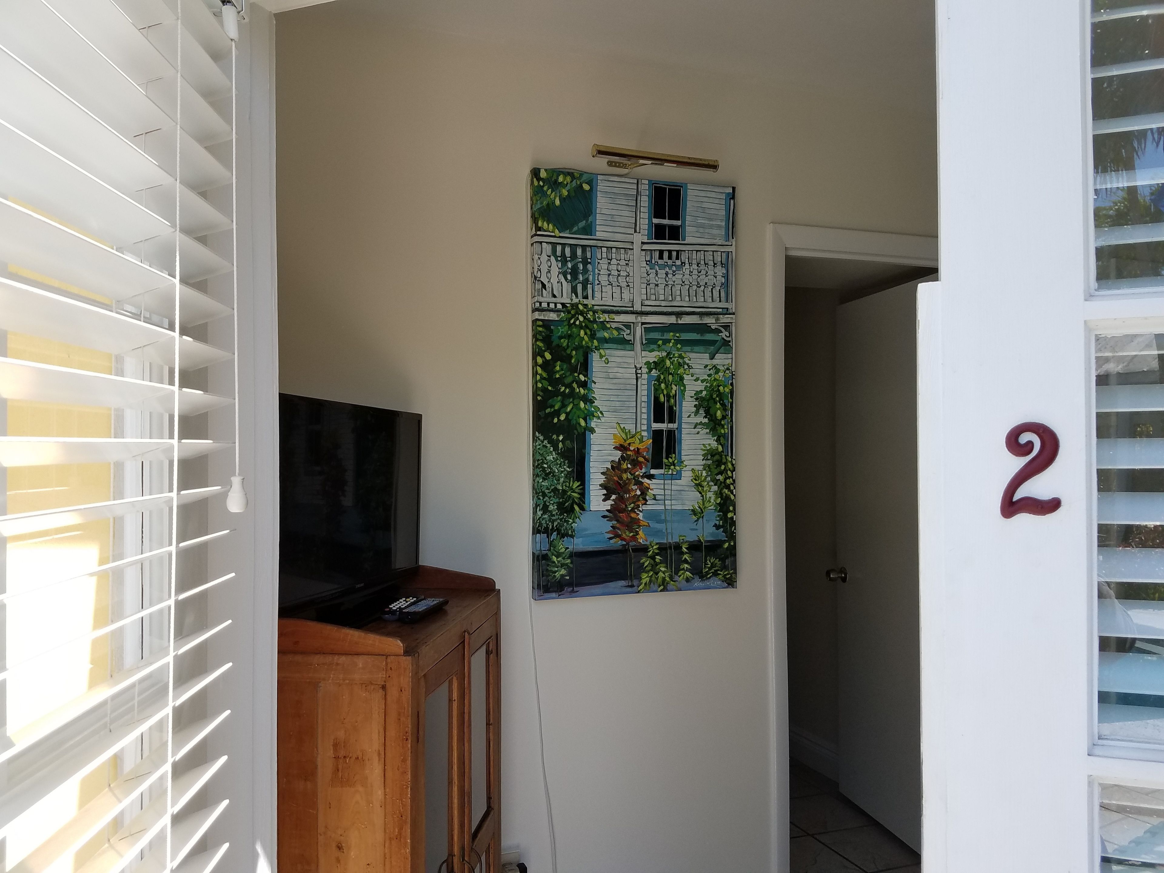 Um corredor com um armário de madeira, uma TV de tela plana e um quadro na parede retratando uma casa.