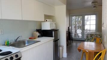 A compact kitchen with a stove, sink, and refrigerator, a dining area with a table and chairs, and a view through a glass door to an outdoor area.