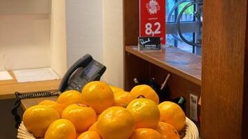 Un panier en osier rempli d’oranges est posé sur un comptoir en bois. On aperçoit, à l’arrière-plan, un panneau rouge portant le chiffre 8,2, un téléphone et une cloche.