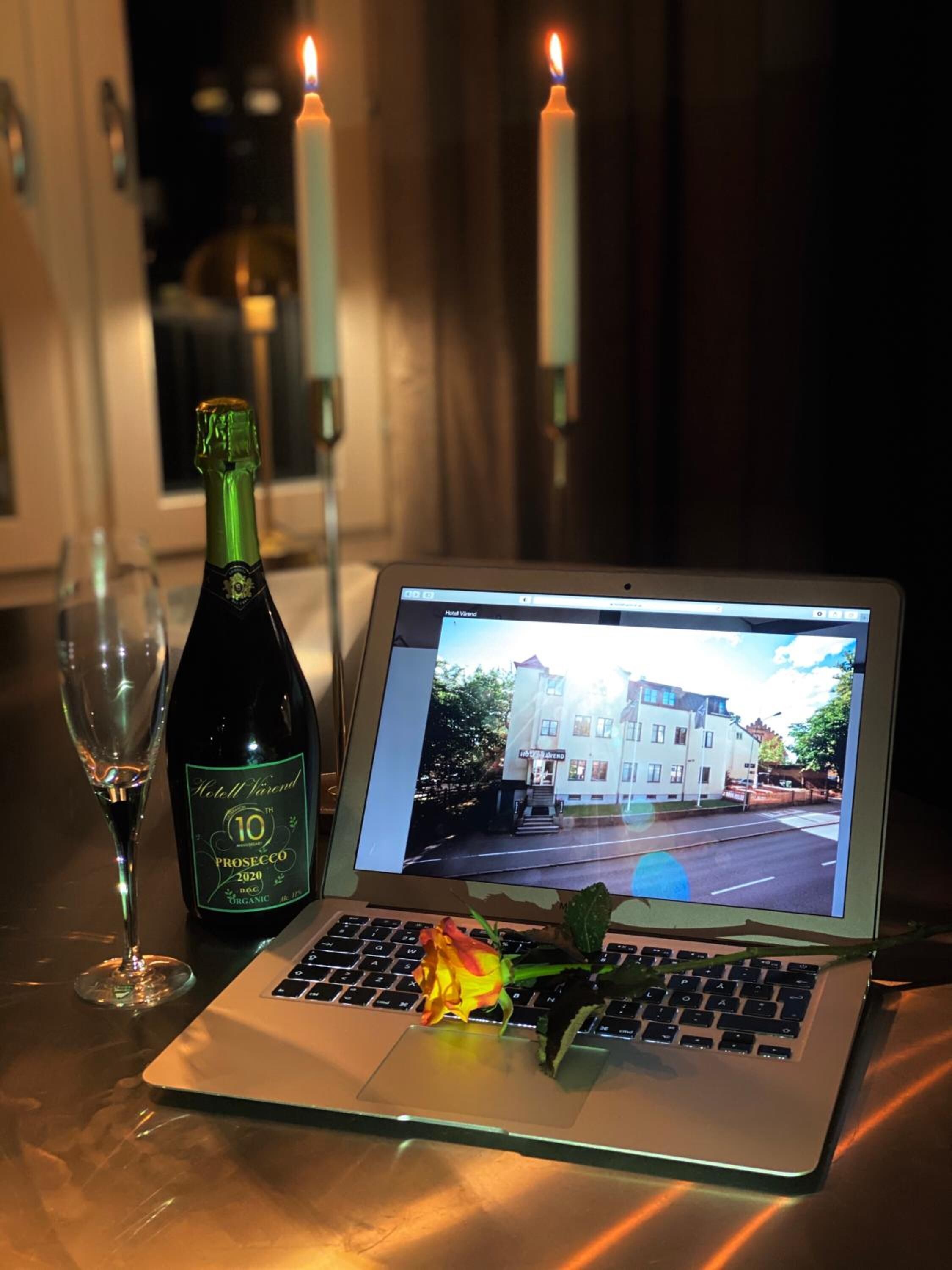 A laptop on a table with a bottle of wine, a glass, and a rose.