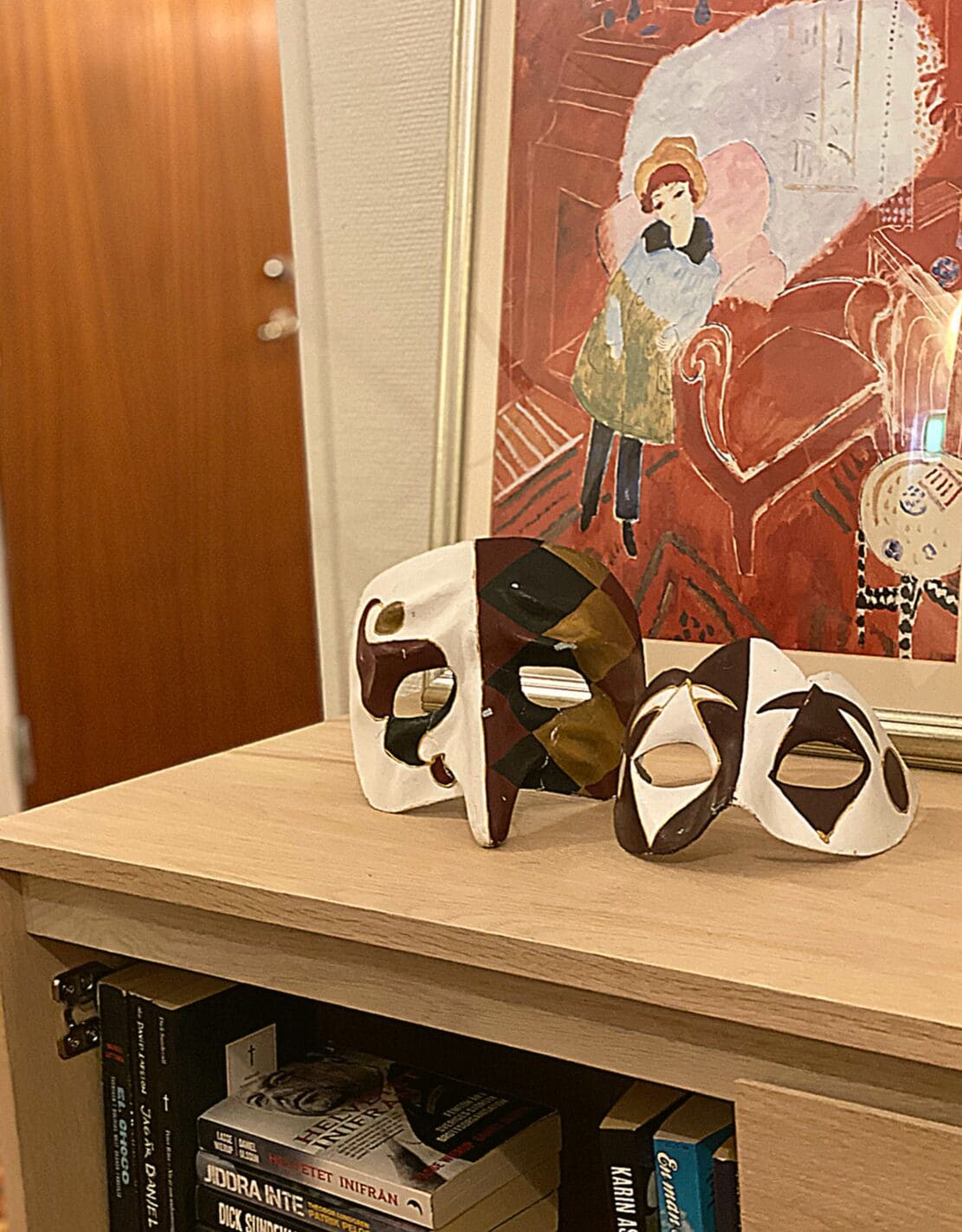 Ein Holzregal mit drei Masken und einem gerahmten Kunstwerk.