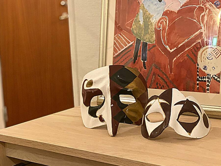 Ein Holzregal mit drei Masken und einem gerahmten Kunstwerk.