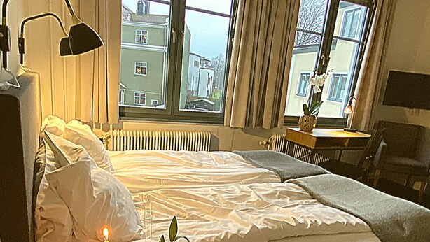 A bedroom with a bed, two windows, a radiator, a desk, a chair, and a plant. - Hotell Värend (Växjö)