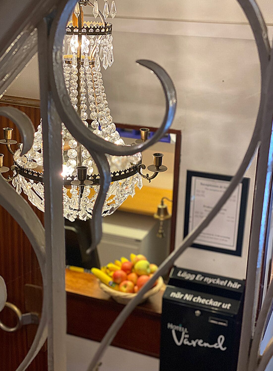 A chandelier with crystal decorations and a sign in a room with a wooden floor and a fruit bowl.