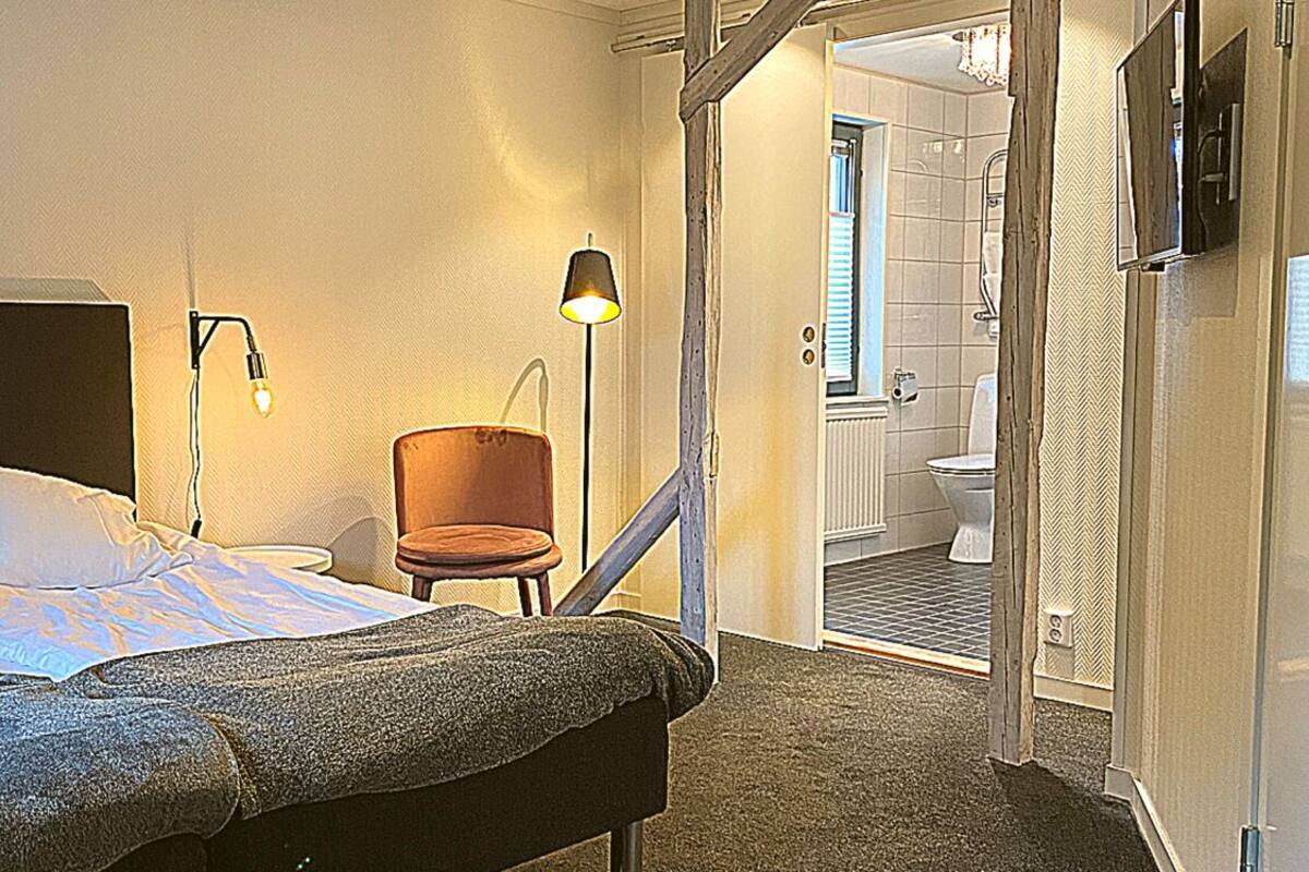 A hotel room with a bed, a chair, a lamp, and a view of the bathroom.