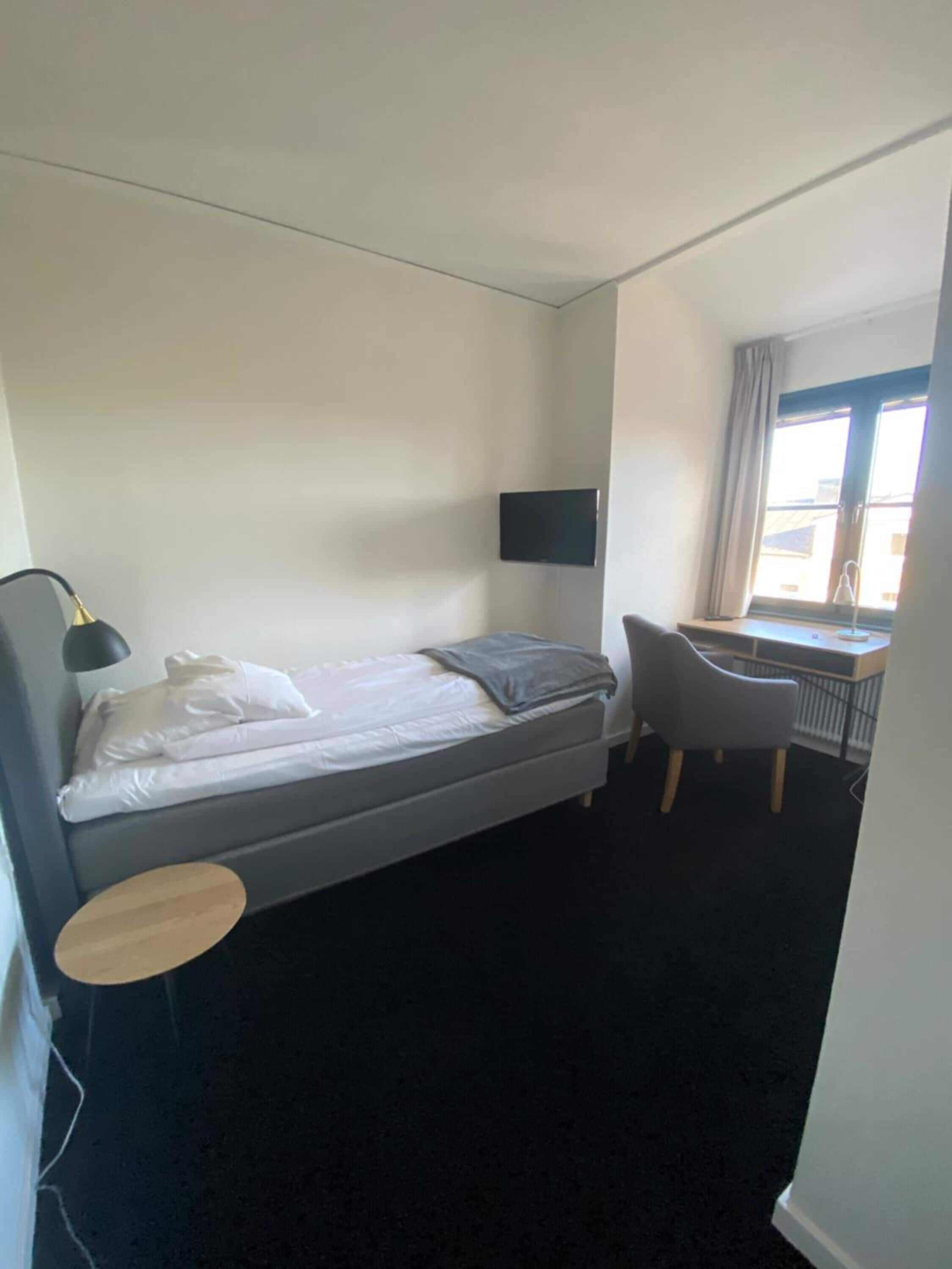 Una habitación de hotel con una cama, un escritorio, una silla, un televisor y una ventana.