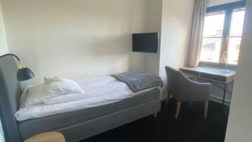 A hotel room with a bed, a desk, a chair, a TV, and a window.