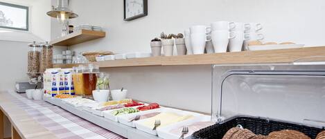 A breakfast buffet with various food items and utensils, a clock on the wall, and a window providing natural light.