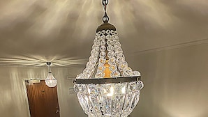 A room with a chandelier, a wooden door, a patterned carpet, a wooden cabinet, and a table lamp. - Hotell Värend (Växjö)