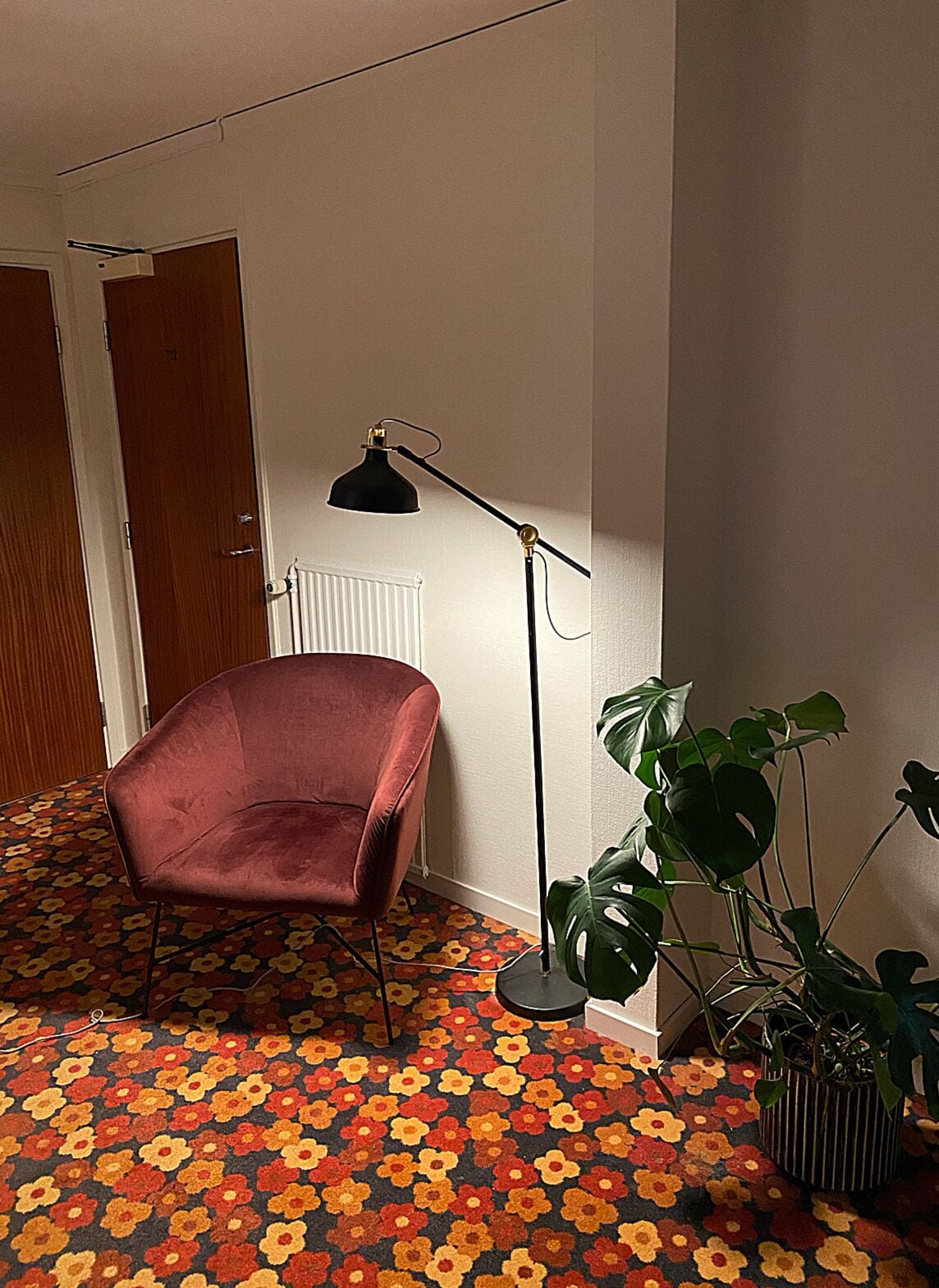 A room with a red velvet chair, a floor lamp, and a potted plant.